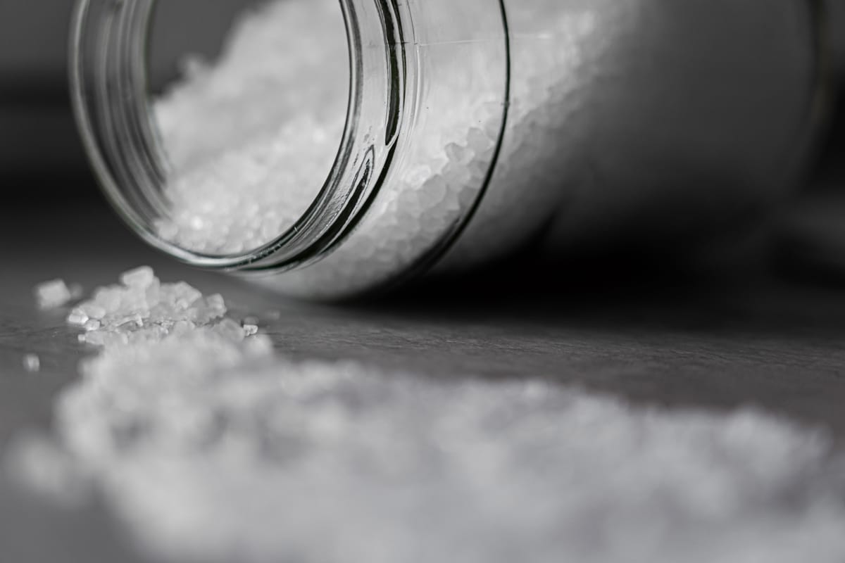Black-and-white close-up of salt crystals spilling from a glass jar onto a tabletop
